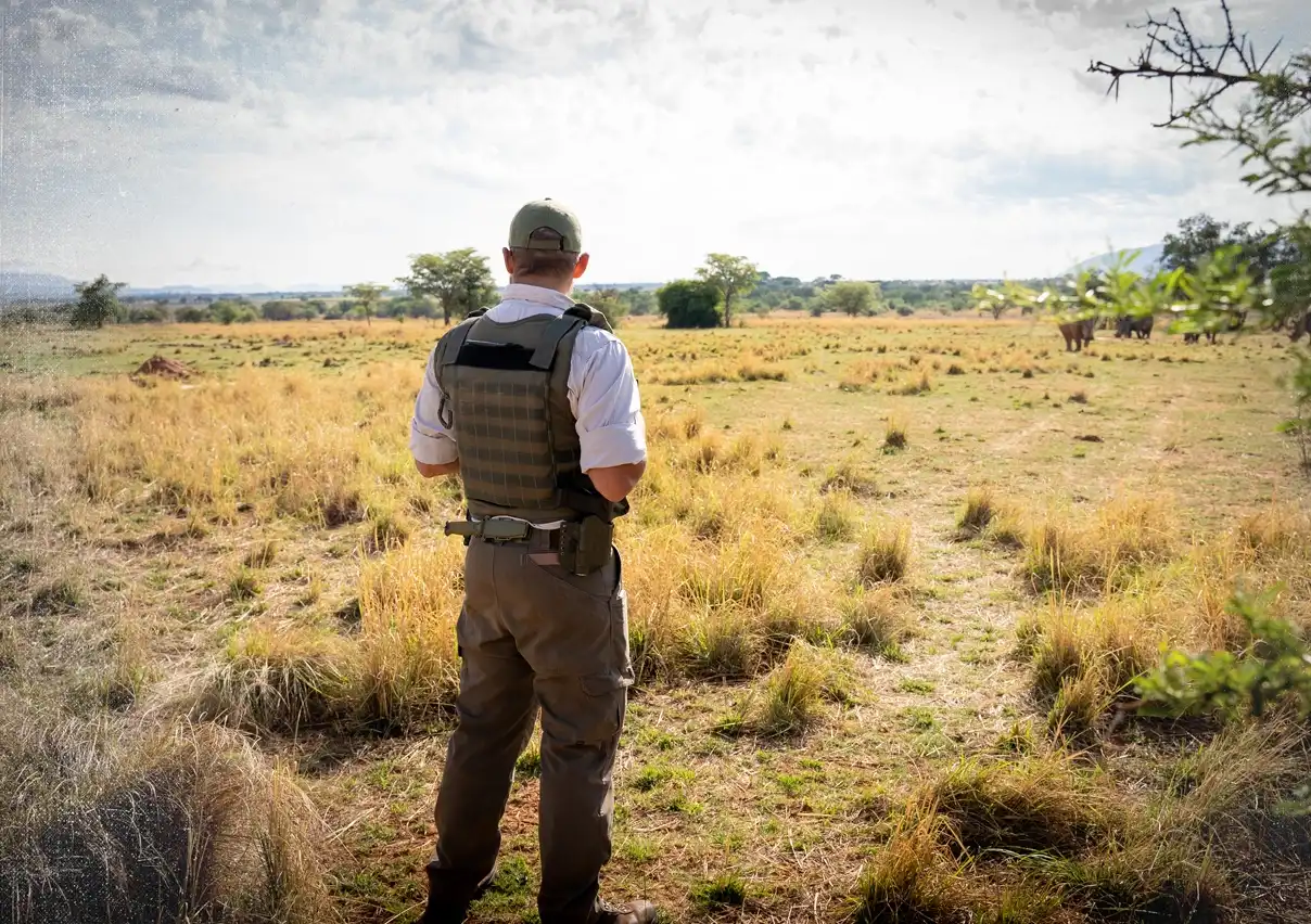 Anti-Poaching-Unit-Mitglied mit kugelsicherer Weste steht in der Savanne, den Rücken zur Kamera gewandt