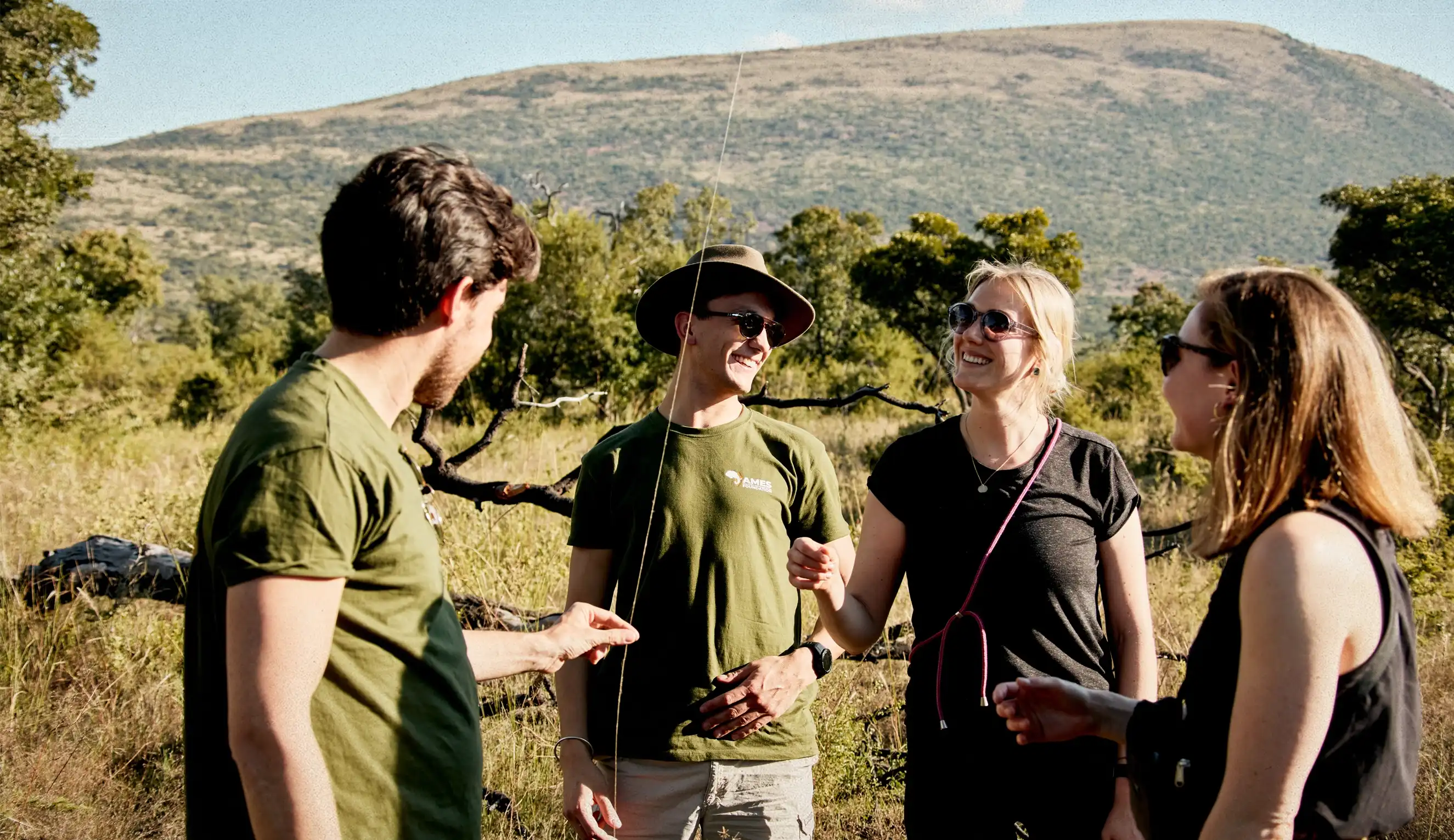 Eine Gruppe lächelnder AMES-Mitglieder in der Sonne, die sich unterhalten und einen Grashalm begutachten.