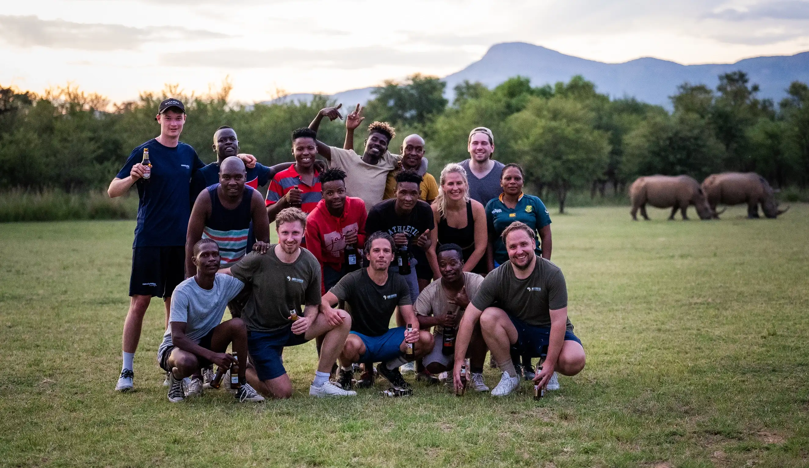 Large team posing with drinks, while two rhinos graze in the background