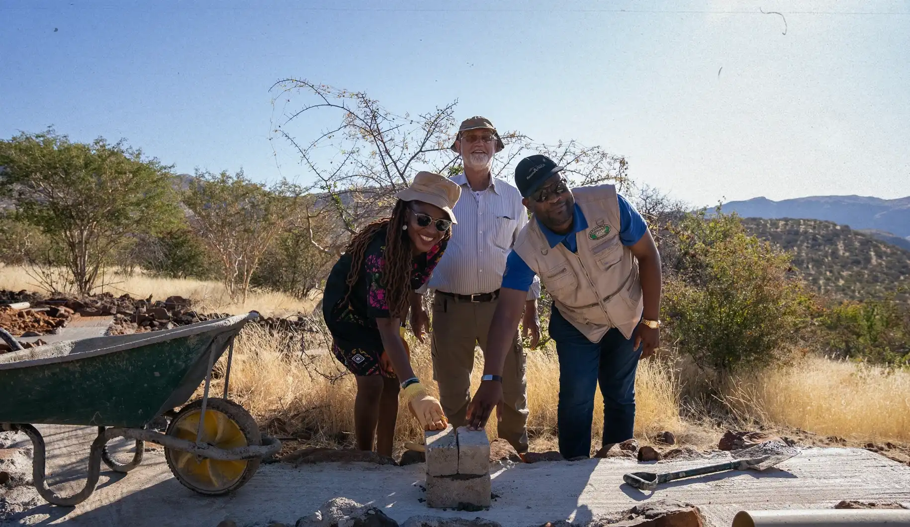 3 people on construction site laying the foundation stone of a research centre in the savanna