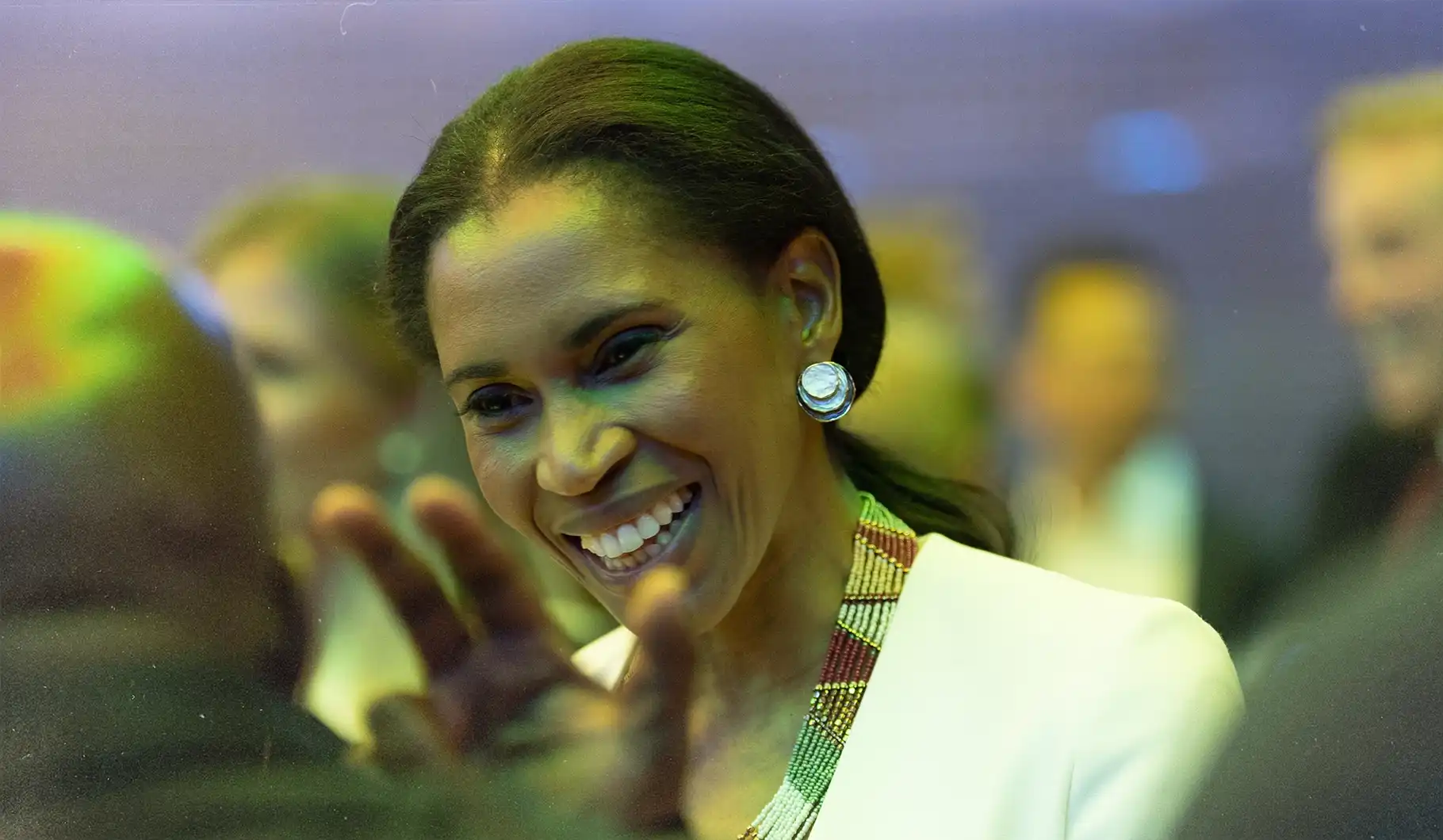 Smiling attendee wearing a colorful beaded necklace and large earrings holding a conversation at the South African Embassy.